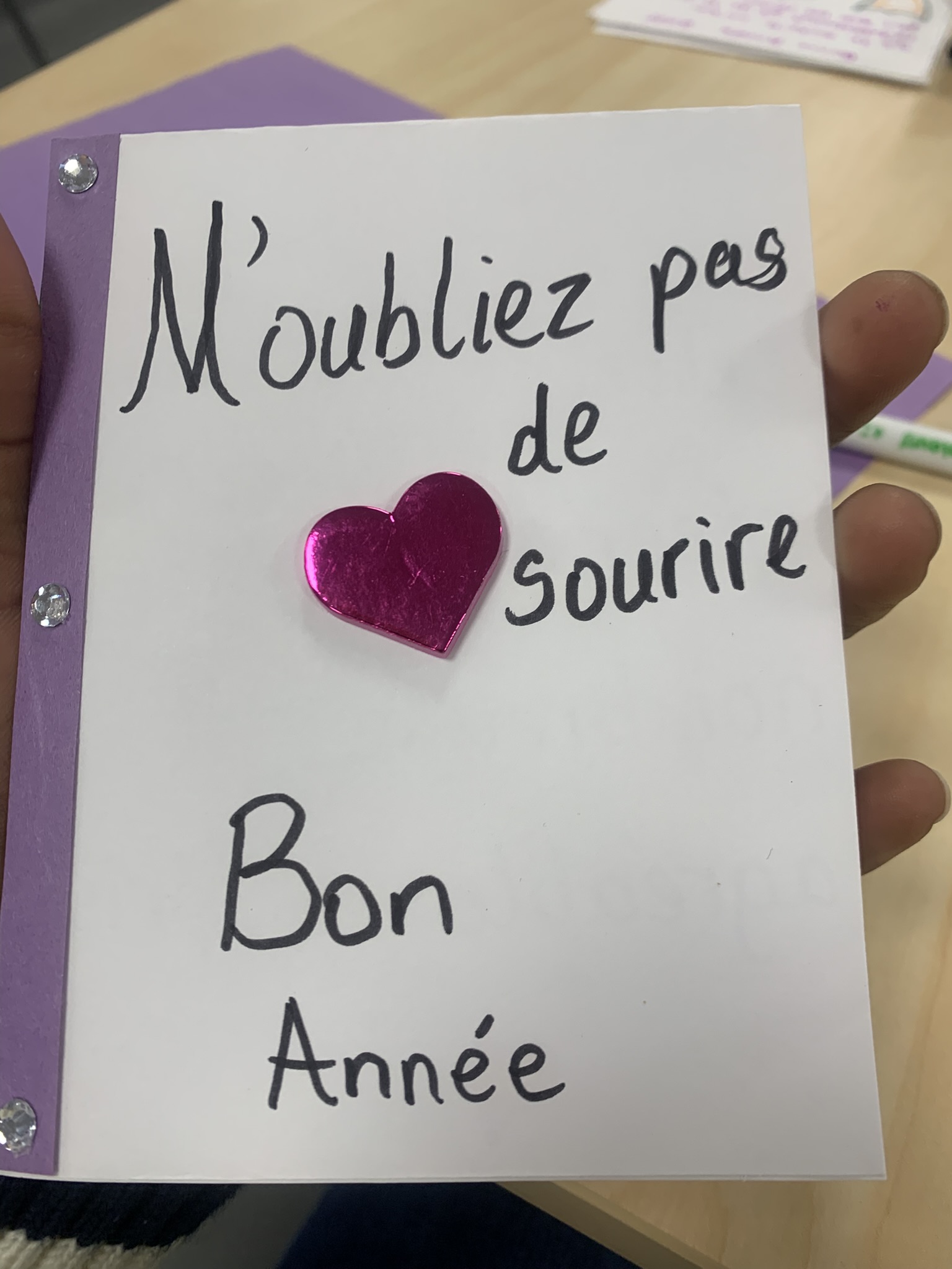 Handmade New Year's card with purple background reading 'N'oubliez pas de sourire - Bon Année' with a pink heart decoration